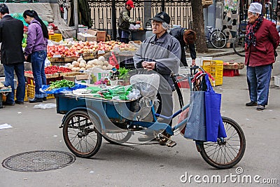 Old lady sells celery off blue tricycle on market. Editorial Stock Photo