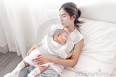 Being mom is so exhausted. Tired mother laid in bed with newborn baby at night. Authentic real life exhausted parent taking rest Stock Photo