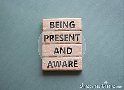 Being Present and Aware symbol. Wooden blocks with words Being Present and Aware. Doctor hand. Beautiful grey green background. Stock Photo