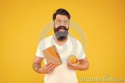 Being proud of geek in you. Geek man. Bearded man in geek glasses holding orange and book on yellow background. Hipster Stock Photo