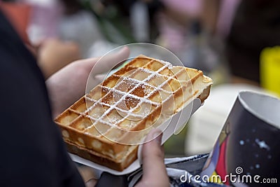 Belgian fresh warm waffle with powdered sugar in hands of buyer. Gastronomic dainty products on market counter, real Stock Photo