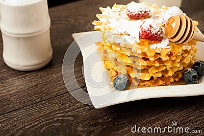 Belgian waffles with raspberries and sieving sugar powder and honey served with jug of milk on a white table Stock Photo