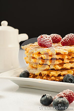 Belgian waffles with raspberries and sieving sugar powder and honey served with jug of milk on a white table Stock Photo