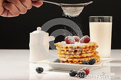 Belgian waffles with raspberries and sieving sugar powder and honey served with jug of milk on a white table Stock Photo