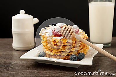 Belgian waffles with raspberries and sieving sugar powder and honey served with jug of milk on a white table Stock Photo