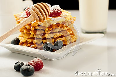 Belgian waffles with raspberries and sieving sugar powder and honey served with jug of milk on a white table Stock Photo