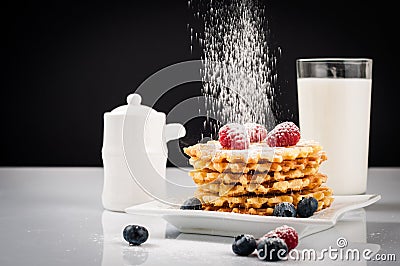 Belgian waffles with raspberries and sieving sugar powder and honey served with jug of milk on a white table Stock Photo