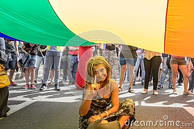 Female pride participant sitting and pointing at a giant rainbow gay flag during the Belgrade Gay Pride. Editorial Stock Photo