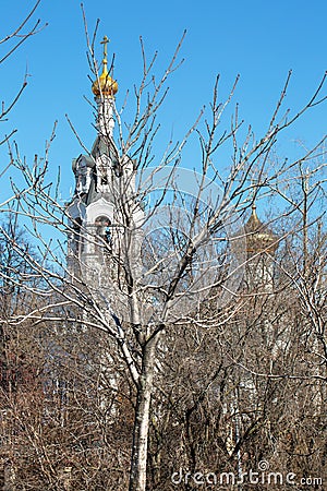 The bell tower of an Orthodox church in Moscow behind thickets of bushes against a blue sky Stock Photo