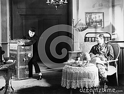 Bellboy struggling with trunk in guests room Stock Photo