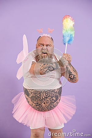 Bellicose obese person in fairy suit attacks with dust brush on purple background Stock Photo
