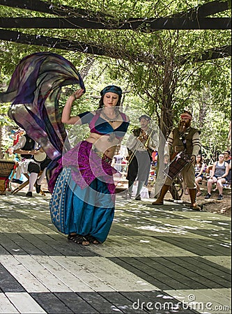 Belly dancer in motion with costumed musicians in vine covered alcove at Renassiance Festival in Muskogee Oklahoma USA 5 28 2017 Editorial Stock Photo