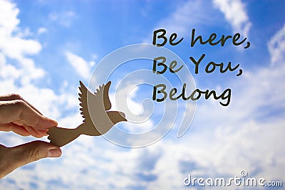 Belong symbol. Man hand holding wooden bird on cloud blue sky background. Words `be here, be you, belong`. Business, belonging a Stock Photo