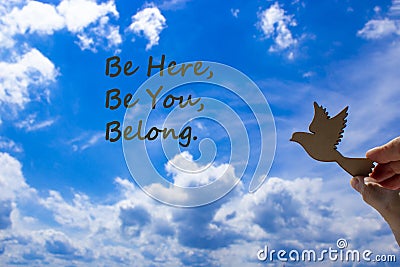 Belong symbol. Man hand holding wooden bird on cloud blue sky background. Words `be here, be you, belong`. Business, belonging a Stock Photo