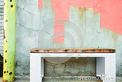 Bench on sidewalk against colorfully painted cement cracked wall. Stock Photo