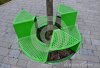 Bench sitting with a hole around a tree. green painted metal perforated plate. three places around the tree around like a pizza or Stock Photo