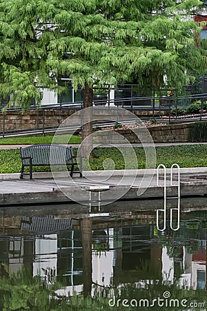 The Woodlands, Texas USA - July 11, 2021: A green bench under a cypress tree on the Waterway. Editorial Stock Photo