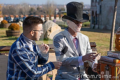 Organ grinder in a hat and round glasses gives an interview on an autumn sunny day in the Editorial Stock Photo