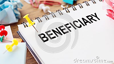 BENEFICIARY word in a notepad on wooden desk with crumpled paper and paper needles around Stock Photo