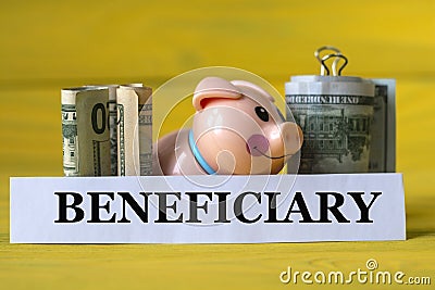 BENEFICIARY - word on a white strip of paper on a piggy bank pig on a yellow background with banknotes Stock Photo