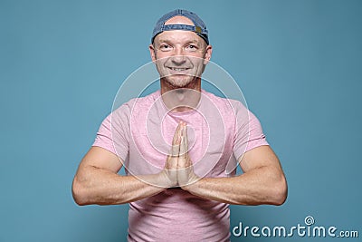 Benevolent, smiling man folded hands in a namaste gesture. Blue background. Stock Photo