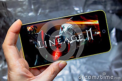 Berdyansk, Ukraine - March 16, 2019: Hands holding a smartphone with lineage 2 revolution game on display screen Editorial Stock Photo