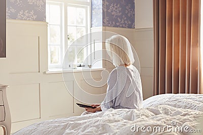 Bereaved Senior Woman Sitting On Edge Of Bed Looking At Photo In Frame Stock Photo