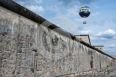 Berlin, Germany - April 2016: Young boy with ball looks through damaged section of the Berlin Wall. Editorial Stock Photo