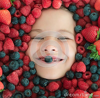 Berries child face close up. Top view photo of child face with berri. Berry set near kids face. Cute little boy eats Stock Photo