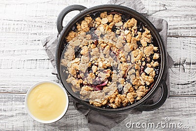 Berry fruit crumble baked with apples and blueberries served with vanilla sauce close-up in a pan. Horizontal top view Stock Photo