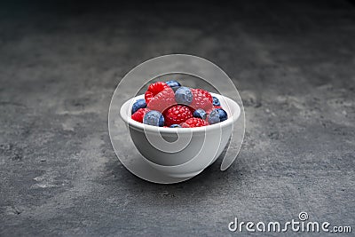 Berry fruit in white ceramic bowl on dark concrete background. Stock Photo