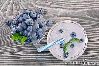 Berry smoothie or yogurt in glass and blueberries in bowl on wooden table Stock Photo