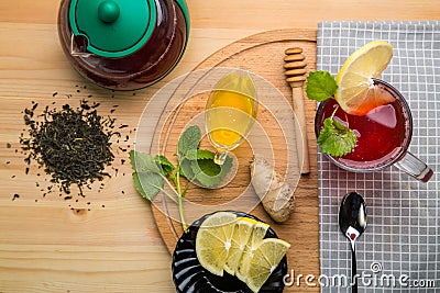 Berry tea in a cup near lemon, honey, lemon balm, ginger and a teapot on a table on a round wooden stand top view. Stock Photo