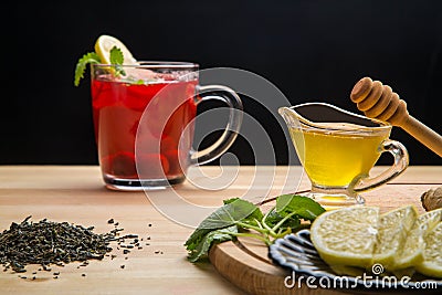 Berry tea in a cup next to lemon, honey, lemon balm and a teapot with a drink on the table. Stock Photo