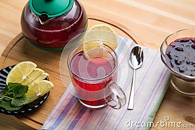 Berry tea in a cup next to lemon, honey, lemon balm, ginger and a teapot on the table on a round wooden stand. Stock Photo