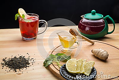 Berry tea in a cup next to lemon, honey, lemon balm and a teapot with a drink on the table. Stock Photo