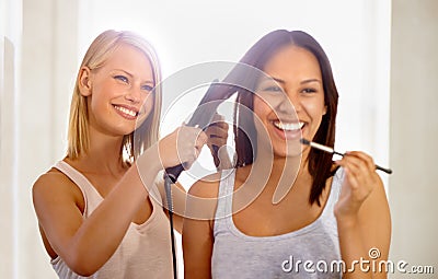 The best friend a woman can have. a young woman applying makeup while her friend straightens her hair. Stock Photo