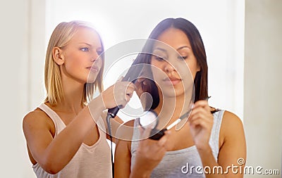 Best friends help each other to look their best. a young woman applying makeup while her friend straightens her hair. Stock Photo
