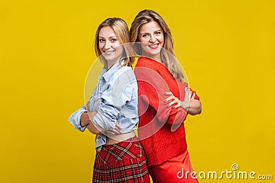 Best friends standing with their backs to each other. Portrait of two happy charming women, isolated on yellow background Stock Photo