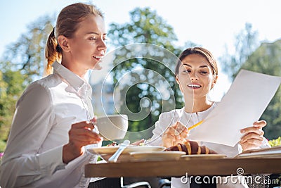 Pleasant woman explaining data on printouts to colleague in cafe Stock Photo