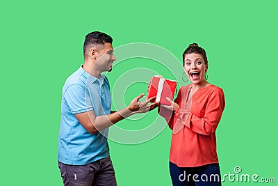 Best present for woman. Young handsome man in casual clothes giving gift box to pleasantly surprised woman. isolated on green Stock Photo