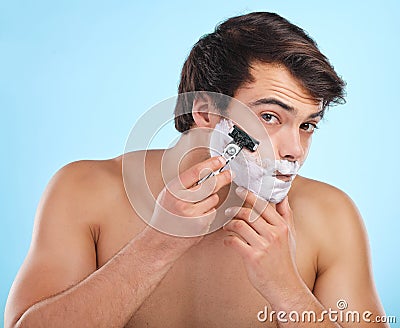 The best shave a man can get. a young man shaving his face against a studio background. Stock Photo