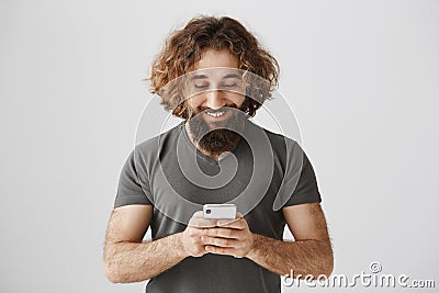 Best way of communication. Portrait of pleased and concentrated eastern male holding smartphone, playing games or Stock Photo