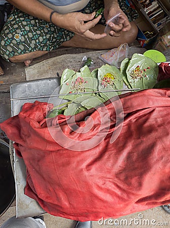 Betel leaves or mitha paan being prepared with ingredients like areka nut or supari and other condiments in a shop for sale in Stock Photo