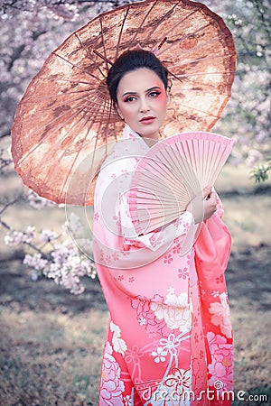 Beuatiful girl with japanese traditional kimono and umbrella in orchard during spring Stock Photo