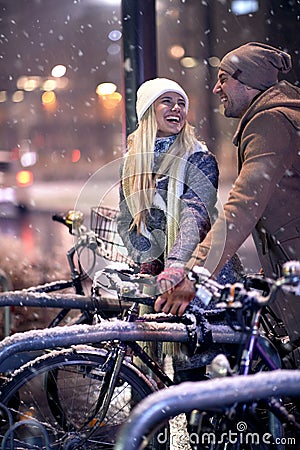 Beutiful blonde with long hair looking her boyfriend, laughing about riding bicycles while snowing. christmastime concept Stock Photo