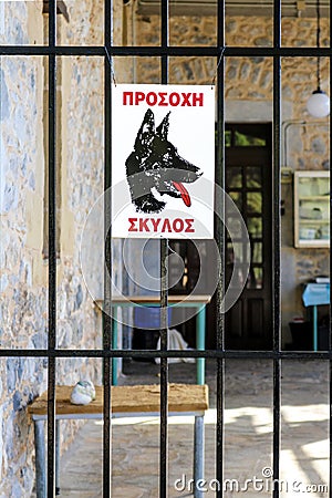Beware of dog sign in Greek language on metal fence to outdoor rock entryway with tables - inside blurred behind bars Stock Photo