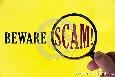 Beware scam text on yellow cover with hand holding magnifying glass. Scamming and fraud concept Stock Photo