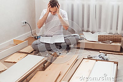 Bewildered man assembling new wooden furniture at home. Man reading instructions and misunderstand what to do the next. Stock Photo