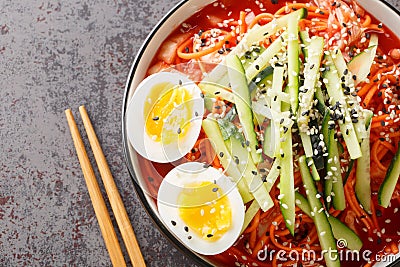 Bibim-guksu Korean spicy Noodles salad with kimchi, cucumber and eggs closeup in the bowl. Horizontal top view Stock Photo